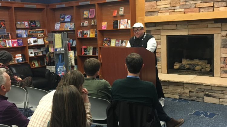 Hieu Minh Nguyen stands at a podium and recites poetry to an audience in the Wolf Shop.