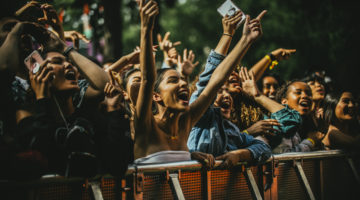 Crowd of fans press toward the barrier at the front of a concert while cheering for a performer.