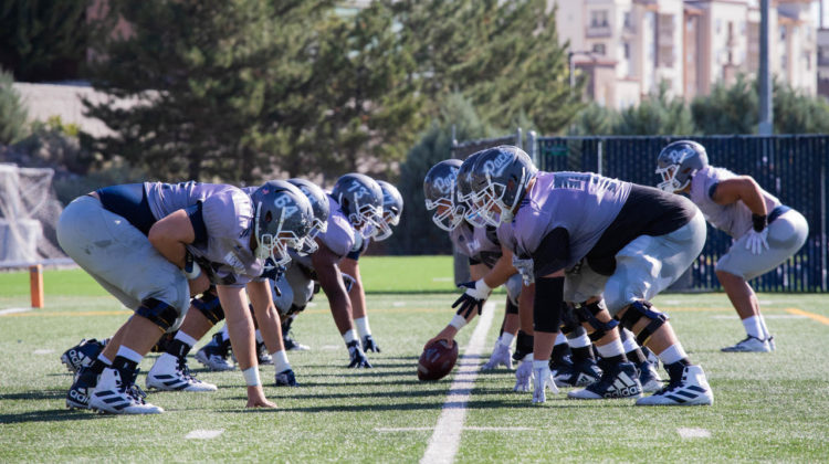 Nevada football's linemen prepare to do battle against each other. On the left side of the line, four players prepare to line up against five other linemen. Only three of the five offensive players are visible.