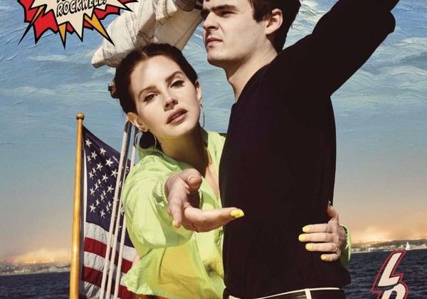 A woman and a man are on a ship. The brunette woman is wearing a green shirt and is reaching her hand out. The man has brown hair, is wearing khakis and a long-sleeved black shirt. There is an American flag in the background with the words "Norman Fucking Rockwell!"