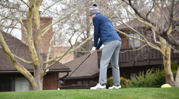Golfer Mitch Abbott practices his golf swing on the course. Abbott is wearing grey pants, blue top and a Nevada beanie.