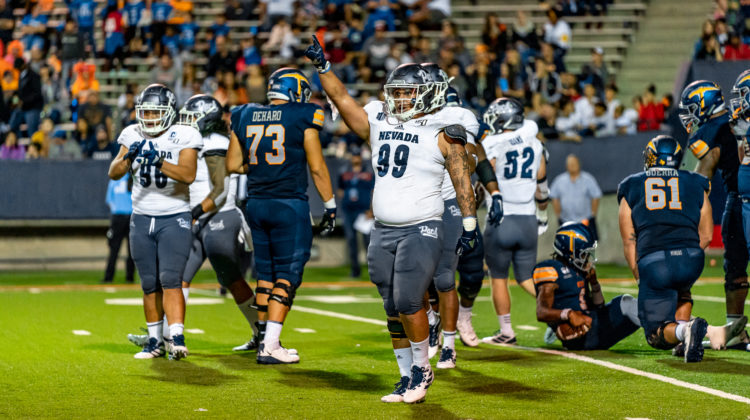 Nevada football player Dom Peterson celebrates after a play on September 21, 2019. Peterson is wearing grey pants and a white No. 99 jersey.