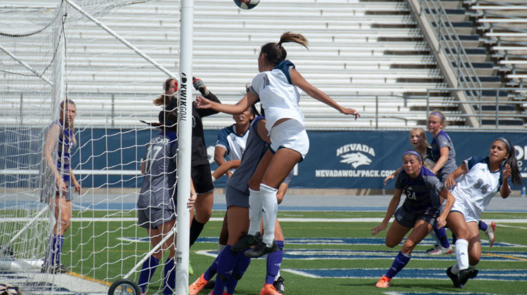 A Nevada defender leaps into the air in an attempt to head the ball. She wears both a white jersey and shorts. Her number is unclear.