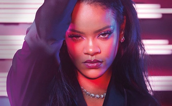 This Amazon Prime promotional poster shows Rihanna in a black blazer, diamond necklace and half-up-half-down styled long black hair. She is behind a pink and purple background with lights. The bottom of the poster says "Savage X Fenty Show."