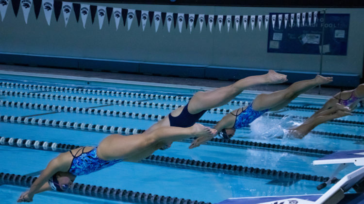 Five Nevada swimmers are seen diving into the Lombardi Pool on Sept. 21, 2019. Each swimmer is wearing a different uniform ranging from light blue, camo and dark navy.