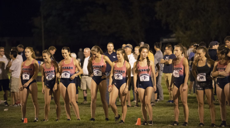 The women of Nevada cross country line up to begin The Bonanza Casino Nevada Twilight Classic. All of Nevada's runners are wearing pink and blue jerseys/running shorts. Nine runners in total are pictured.