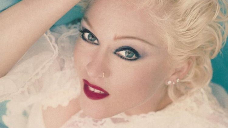 Madonna is laying on a teal colored sheet wearing a white laced long sleeve shirt. She has short, curly blonde hair and has her right hand on her head. The name "Madonna" is written in pink up top and the title "Bedtime Stories" is written in teal across the bottom.