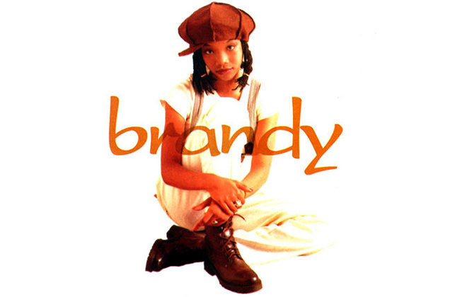 A girl sitting on the ground with her arms around her knee. She has black shoulder-length hair, an orange-brown hat, a white t-shirt and khakis. The name "brandy" is written across in orange font.