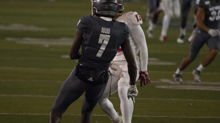 Romeo Doubs runs a route against a New Mexico defender. Doubs, No. 7, wears an all grey uniform while the New Mexico player wears all white with red accents.