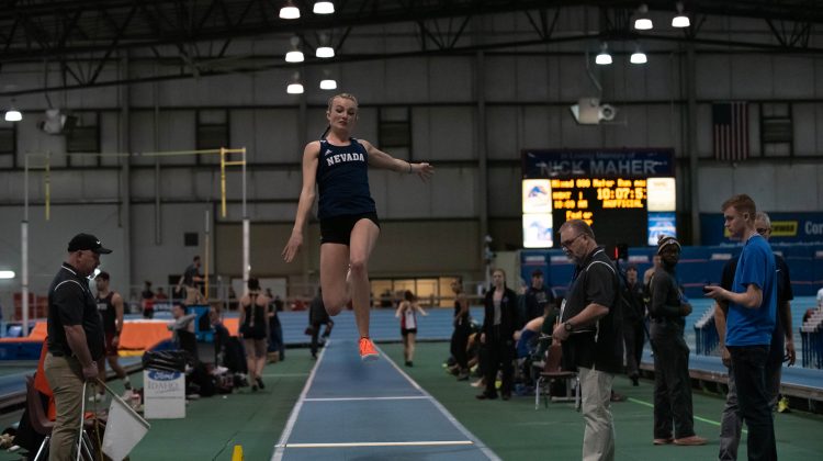 Hanah Smrt leaps through the air during the long jump portion of the pentathlon. Smrt is wearing a blue top with "Nevada" written on it, and black shorts.