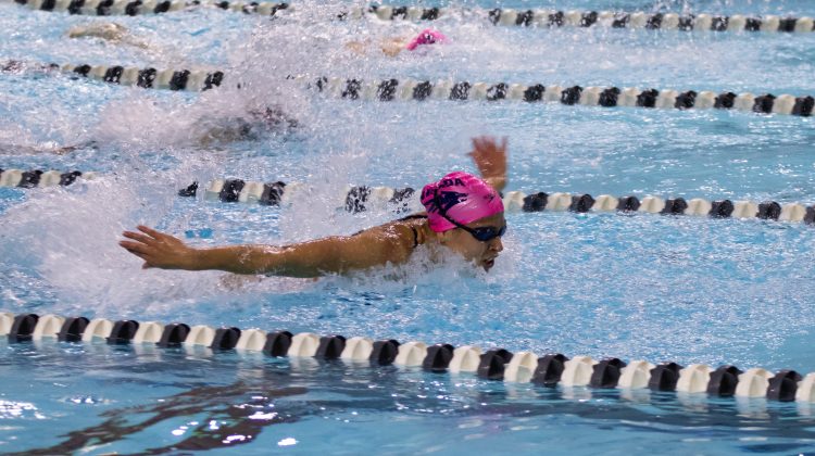 A Nevada swimmer competes in a race during a heat against New Mexico. The swimmer is wearing a pink swim cap.