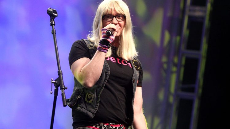 Liam Kyle Sullivan as Kelly, wearing a blonde wig and black glasses, performs on stage at VidCon.