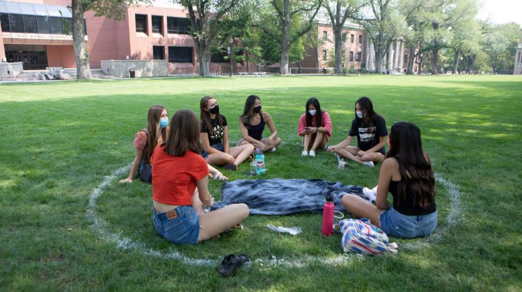 A group of seven masked students sit on the Quad in Aug. 2020.