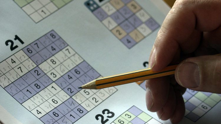 A hand holding a pencil is working on sudoku puzzles