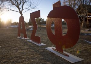Red, wooden Greek letters representing "Alpha Sigma Phi" stand at an Alpha Sigma Phi rush event.