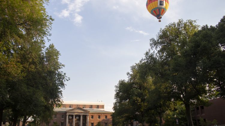 Colorful air balloon in the sky over the tree lines hovering over the university.