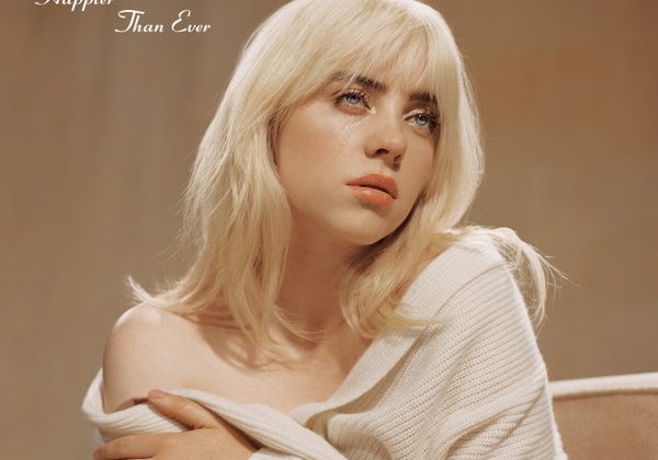 Blonde Billie Eilish holding her shoulders with a white baggy sweatshirt around her in a brown background with her album title in cursive next to her.