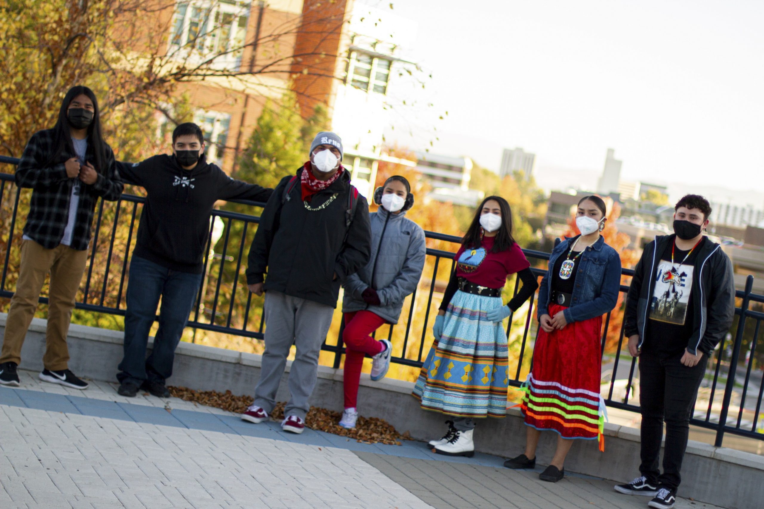 Seven individuals stand against a railing, downtown Reno can be seen in the distance