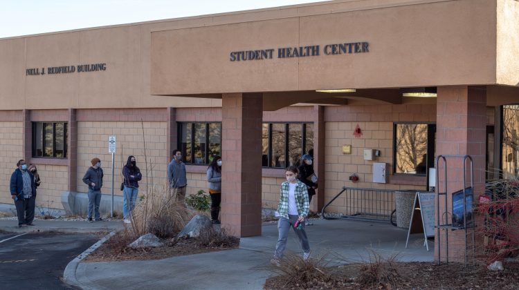 People lined up in front of an orange building that reads Student Health Center