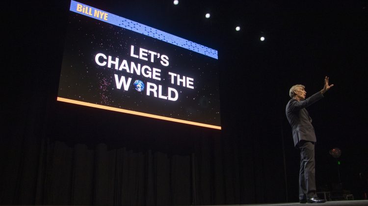 Bill Nye stands in front of a slide that reads Let's Change the World